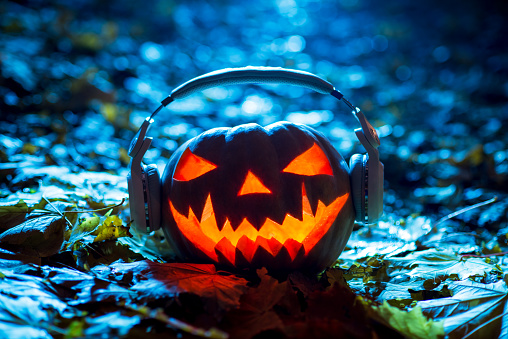 pumpkin head jack with headphones in autumn forest at night on leaves, halloween music