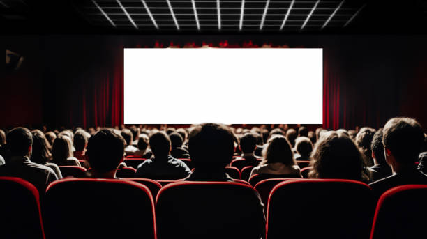 Cinema blank screen and people in red chairs in the cinema hall. Blurred People silhouettes watching movie performance.